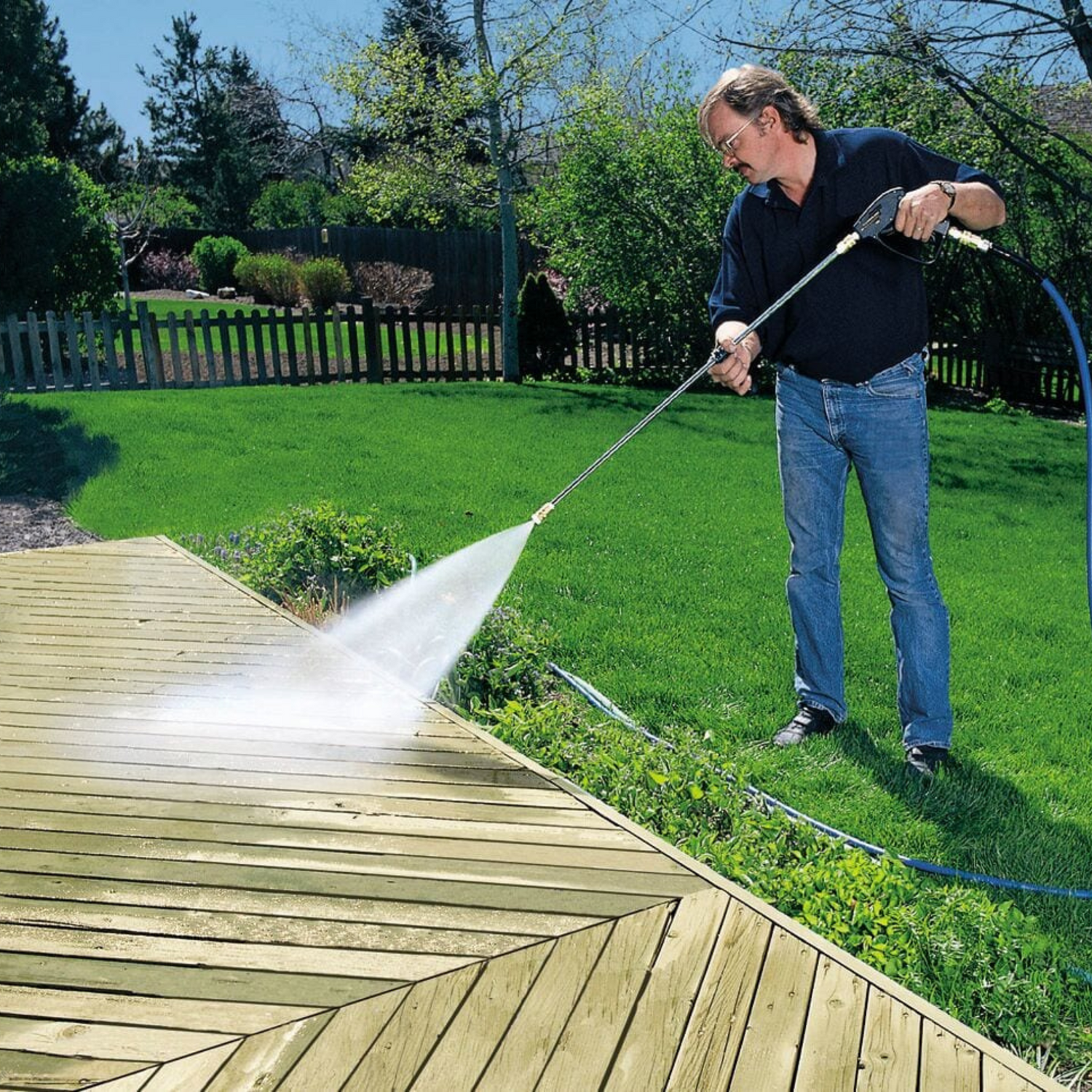 Man in jeans and polo power washing a deck