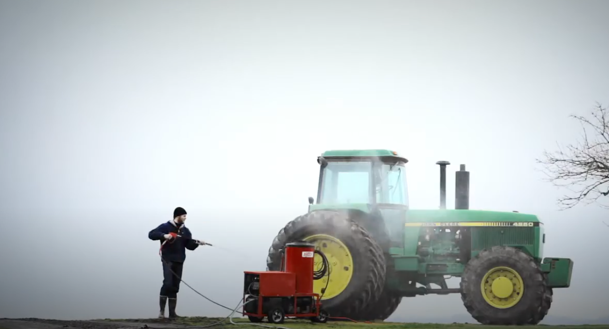 Man in cold weather gear pressure washing a tractor